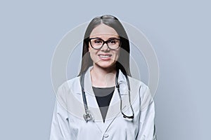 Portrait of smiling female doctor looking at camera on grey background