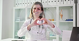 Portrait of smiling female doctor looking at camera, showing finger heart sign