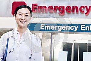 Portrait of smiling female doctor outside of the hospital, emergency room sign in the background