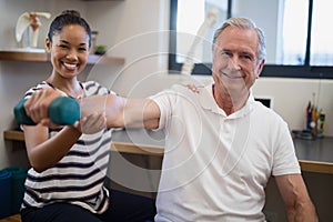 Portrait of smiling female doctor with senior male patient holding dumbbell