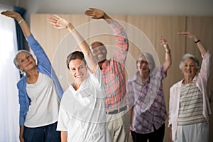 Portrait of smiling female doctor and seniors exercising with arms raised