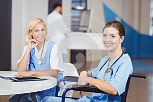 Portrait of smiling female doctor sitting on wheelchair with colleagues