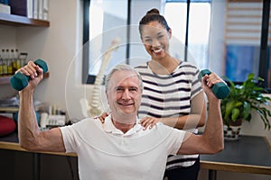 Portrait of smiling female doctor standing with male patient lifting dumbbells