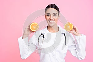 Portrait of smiling female doctor with stethoscope holding oranges isolated.