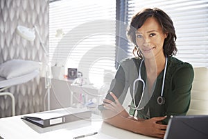 Portrait Of Smiling Female Doctor With Stethoscope Sitting Behind Desk In Office