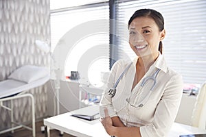 Portrait Of Smiling Female Doctor With Stethoscope Standing By Desk In Office