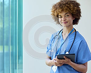 Portrait Of Smiling Female Doctor Wearing Scrubs With Digital Tablet In Hospital