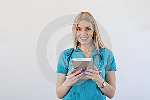 Portrait Of Smiling Female Doctor Wearing Scrubs In Hospital Corridor Holding Digital Tablet