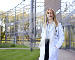 Portrait Of Smiling Female Doctor Wearing White Coat Standing Outside Modern Hospital Building