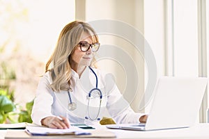 Portrait of smiling female doctor working on her laptop in doctor`s office