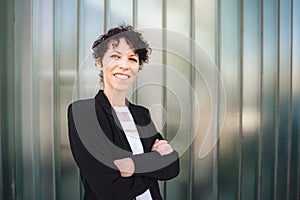 Portrait of smiling female entrepreneur standing arms crossed against green wall