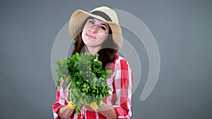 portrait of smiling female farmer in plaid shirt, gloves and hat holding, smells a bunch of fresh green parsley, greens