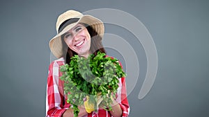 portrait of smiling female farmer in plaid shirt, gloves and hat holding, smells a bunch of fresh green parsley, greens