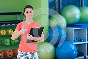 Portrait of smiling female fitness instructor writing in clipboard while standing in gym