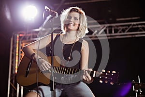 Portrait of smiling female guitarist playing guitar at nightclub