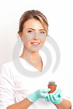 A portrait of a smiling female holds little green cactus in her hands. Hair removal concept.