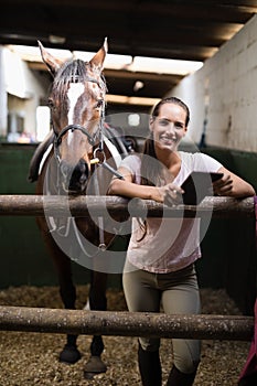 Portrait of smiling female jockey using digital tablet by standing by horse