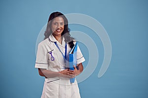 Portrait Of Smiling Female Mature Nurse Wearing Uniform Standing In Front Of Blue Studio Background