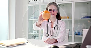 Portrait of smiling female nutritionist doctor holding an orange and recommending fresh fruit