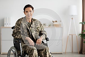 Portrait Of Smiling Female Soldier In Camouflage Uniform Sitting In Wheelchair Indoors