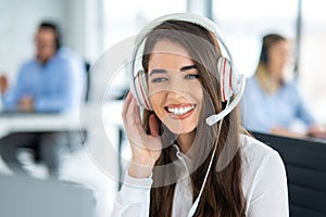 Portrait of smiling female support agent with headset working on computer at call center office.