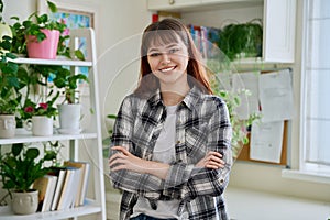 Portrait of smiling female teenager looking at camera with crossed arms in home