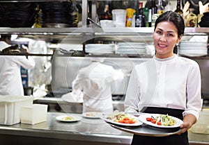 portrait of smiling female waiter standing in kitchen in restaurante