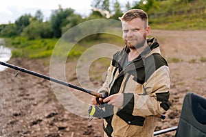 Portrait of smiling fisher man holding spinning casting rod standing on bank waiting for bites on water river at summer