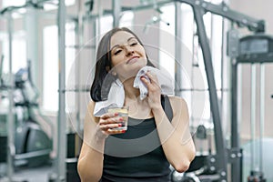 Portrait of smiling fitness woman with glass of water with lemon, woman in sportswear after fitness classes drinking water in gym