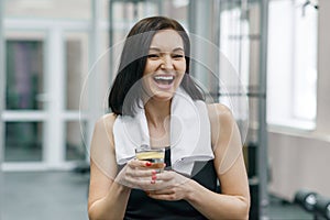 Portrait of smiling fitness woman with glass of water with lemon, woman in sportswear after fitness classes drinking water in gym