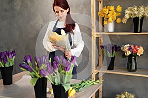 Portrait of a smiling florist owner standing in an apron with a bouquet of yellow tulips near a shop window surrounded