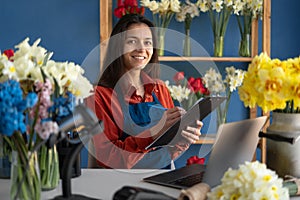 Portrait of smiling florist small business flower shop owner. Woman using her laptop and clipboard to take orders for