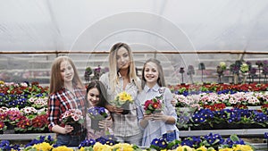 Portrait of smiling four girls stretching synchronously flower pots to camera