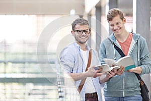 Portrait of smiling friends with books standing at university corridor