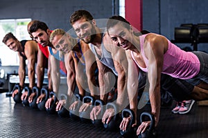 Portrait of smiling friends doing push-ups with kettlebell in gym