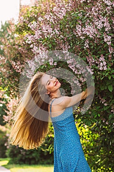 Portrait of smiling girl with blond hair and closed eyes and blue dress among lilac