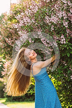 Portrait of smiling girl with blond hair and closed eyes and blue dress among lilac