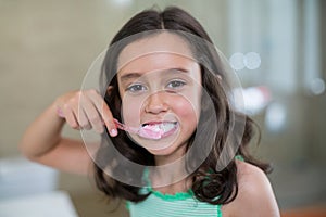 Portrait of smiling girl brushing her teeth in bathroom