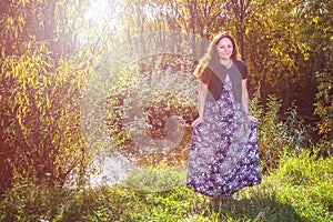 Portrait of a smiling girl in a colored dress illuminated by the rays of the sun in a deciduous forest.