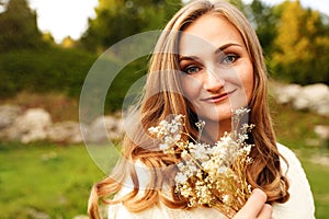 Portrait of a smiling girl with flowers. Blue-eyed blonde on the background of nature