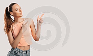 Portrait of a smiling girl pointing finger to the side at on a white isolated background. Positive woman points to an idea, a