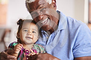 Portrait Of Smiling Grandfather Sitting On Sofa At Home With Baby Granddaughter