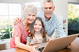 Portrait of smiling grandparents and granddaughter using laptop