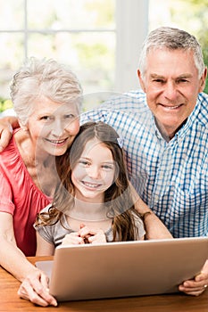 Portrait of smiling grandparents and granddaughter using laptop