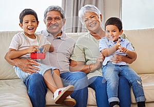 Portrait of smiling grandparents while holding their grandsons on a sofa in the lounge. Senior hispanic man and woman