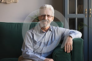 Portrait of smiling elderly man in glasses sitting on couch