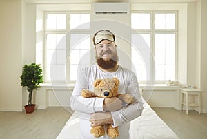Portrait of a smiling grown-up man in pajamas cuddling his teddy bear like a baby