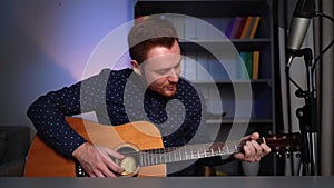 Portrait of smiling guitarist singer male playing acoustic guitar and singing song looking at camera