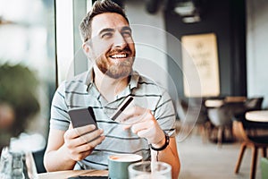 Portrait of smiling guy making online payment with smartphone. Man shopping on mobile phone and paying by credit card