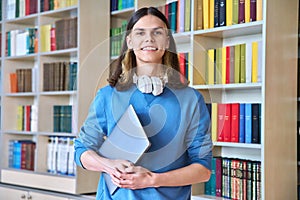 Portrait of a smiling guy student with laptop in hand looking at camera in library